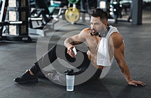 Handsome hot guy resting at gym with phone and water