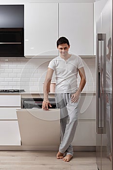 handsome husband man using dishwasher in white modern kitchen