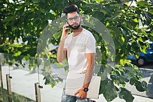 Handsome indian man cell phone call smile outdoor city street. Young attractive businessman casual blue shirt talking