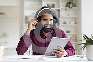 Handsome Indian Man Wearing Wireless Headphones Using Digital Tablet At Home
