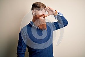 Handsome Irish redhead business man with beard standing over isolated background very happy and smiling looking far away with hand