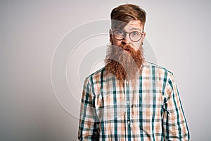 Handsome Irish redhead man with beard wearing glasses and hipster shirt with serious expression on face