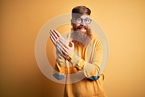 Handsome Irish redhead man with beard wearing glasses over yellow isolated background clapping and applauding happy and joyful,