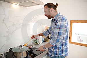 Handsome Italian young adult man standing by a kitchen counter while cooking dinner in minimalist home kitchen