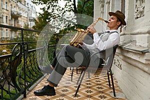 Handsome jazzman enjoys playing saxophone relaxing on terrace