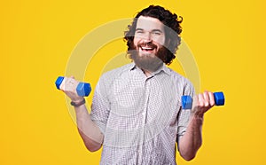 Handsome and joyful man in casual working with small dumbbells