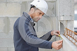 handsome laborer with pencil measuring wall with level tool