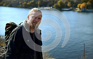 A handsome lamber adventurer smiling at camera and standing on the edge of cliff . A beautiful autumn landscape and lake on