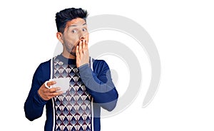 Handsome latin american young man drinking a cup of coffee covering mouth with hand, shocked and afraid for mistake