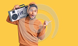 Handsome latin american young man holding boombox, listening to music surprised pointing with finger to the side, open mouth