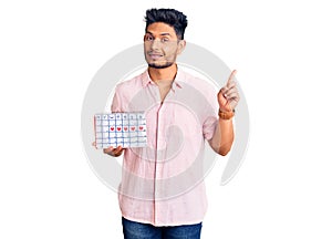 Handsome latin american young man holding heart calendar surprised with an idea or question pointing finger with happy face,