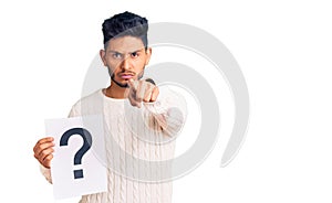 Handsome latin american young man holding question mark pointing with finger to the camera and to you, confident gesture looking