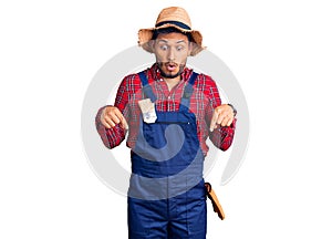 Handsome latin american young man weaing handyman uniform pointing down with fingers showing advertisement, surprised face and