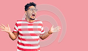 Handsome latin american young man wearing casual clothes and glasses crazy and mad shouting and yelling with aggressive expression