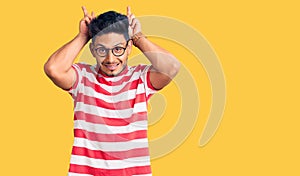 Handsome latin american young man wearing casual clothes and glasses posing funny and crazy with fingers on head as bunny ears,