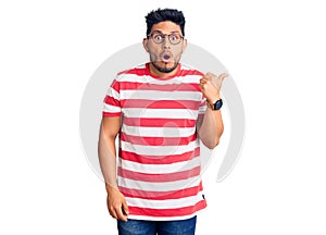 Handsome latin american young man wearing casual clothes and glasses surprised pointing with hand finger to the side, open mouth