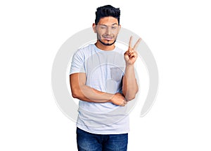 Handsome latin american young man wearing casual clothes smiling with happy face winking at the camera doing victory sign