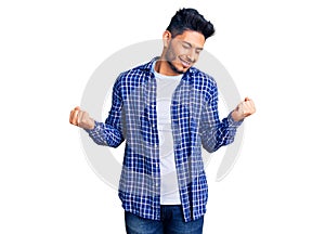 Handsome latin american young man wearing casual shirt very happy and excited doing winner gesture with arms raised, smiling and