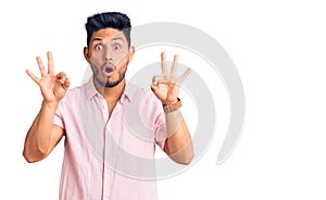 Handsome latin american young man wearing casual summer shirt looking surprised and shocked doing ok approval symbol with fingers