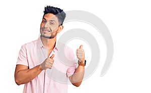Handsome latin american young man wearing casual summer shirt pointing to the back behind with hand and thumbs up, smiling