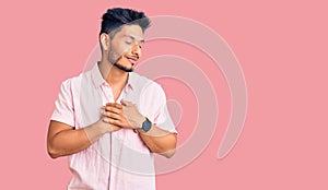 Handsome latin american young man wearing casual summer shirt smiling with hands on chest with closed eyes and grateful gesture on