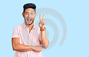 Handsome latin american young man wearing casual summer shirt smiling with happy face winking at the camera doing victory sign