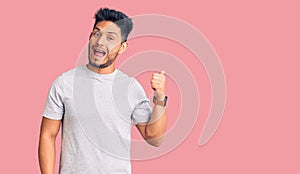 Handsome latin american young man wearing casual tshirt smiling with happy face looking and pointing to the side with thumb up