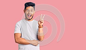 Handsome latin american young man wearing casual tshirt smiling with happy face winking at the camera doing victory sign