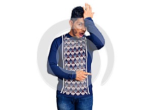 Handsome latin american young man wearing casual winter sweater surprised with hand on head for mistake, remember error