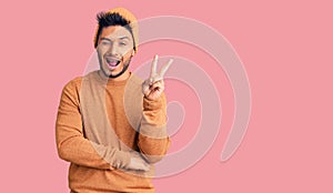 Handsome latin american young man wearing winter sweater and wool hat smiling with happy face winking at the camera doing victory