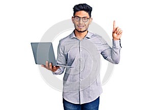 Handsome latin american young man working using computer laptop surprised with an idea or question pointing finger with happy