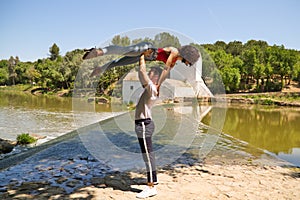 handsome latin man and beautiful latin woman dancing bachata by the river. The man holds the woman horizontally above his head.