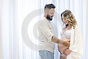 Handsome Latin man and his beautiful pregnant wife, Man holding on his wife`s belly. Curtain background. pregnancy concept