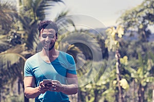 Handsome Latin Man Messaging With Cell Smart Phone Over Tropical Forest Background, Portrait Of Young Guy Chatting