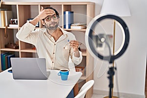 Handsome latin man recording bitcoin tutorial with smartphone at home stressed and frustrated with hand on head, surprised and