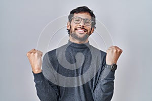 Handsome latin man standing over isolated background celebrating surprised and amazed for success with arms raised and eyes closed