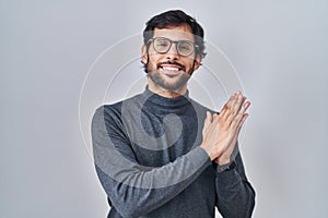 Handsome latin man standing over isolated background clapping and applauding happy and joyful, smiling proud hands together