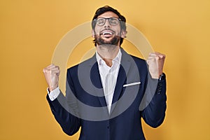 Handsome latin man standing over yellow background celebrating surprised and amazed for success with arms raised and eyes closed