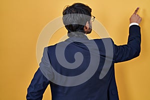Handsome latin man standing over yellow background posing backwards pointing ahead with finger hand