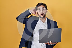 Handsome latin man working using computer laptop crazy and scared with hands on head, afraid and surprised of shock with open