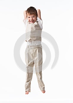 A handsome little boy dressed as a schoolboy - in a white shirt and gray trousers, stands against a white wall and poses