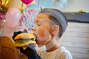 The handsome little boy eating burger in black rubber gloves.