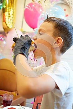 The handsome little boy eating burger in black rubber gloves.