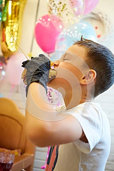 The handsome little boy eating burger in black rubber gloves.