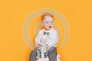 Handsome little boy in front of yellow background in white shirt and bow tie. Kid holding gift flowers for mother in hands