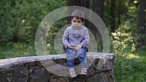 Handsome little boy sits on stone wall and thinks