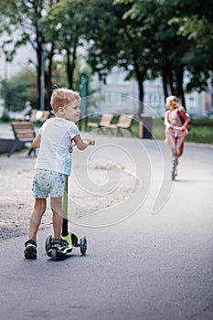 Handsome little boy in stylish shorts rides a scooter on a track in the park on a sunny summer day