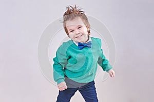 A handsome little boy, wearing a blue bow tie and a green sweater, dances and smiles