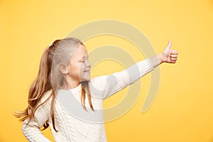 Handsome little girl showing thumb up isolated in the yellow studio.