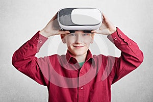 Handsome little male child wears VR glasses, has fun and entertains himself, plays video games, isolated over white background. Sm